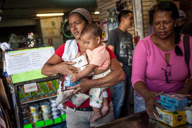 CAR01. CARACAS (VENEZUELA), 16/01/2016.- Una mujer carga a su bebé mientras sostiene productos que compró en un abasto hoy, sábado 16 de enero de 2016, en la ciudad de Caracas (Venezuela). Venezuela, con las mayores reservas probadas de petróleo del mundo, se declaró en emergencia económica para atender la situación del país que después de un año de opacidad reveló una inflación interanual de 141,5 por ciento -la más alta de toda su historia-, y una contracción del 4,5 por ciento. EFE/MIGUEL GUTIÉRREZ
