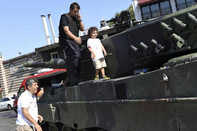 EDITORS NOTE: Graphic content / A child walks next to a police officer on a tank after the military position was taken over at the Anatolian side at Uskudar in Istanbul on July 16, 2016, following an attempt by discontented soldiers to seize power from President Recep Tayyip Erdogan that claimed more than 250 lives. After the bloodiest challenge to his 13-year autocratic rule, Erdogan urged his backers to stay on the streets to prevent a possible "flare-up" of yesterday's chaos in the strategic NATO member of 80 million people. / AFP PHOTO / BULENT KILIC