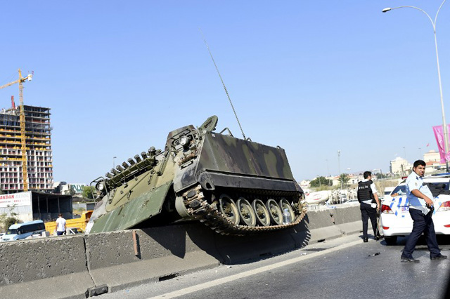 This picture taken on July 16, 2016 shows a tank stucks on a median strip as Turkish police officers walk around it after they took over a military position at the Anatolian side at Uskudar in Istanbul on July 16, 2016. President Recep Tayyip Erdogan urged Turks to remain on the streets on July 16, 2016, as his forces regained control after a spectacular coup bid by discontented soldiers that claimed more than 250 lives. Describing the attempted coup as a "black stain" on Turkey's democracy, Yildirim said that 161 people had been killed in the night of violence and 1,440 wounded. / AFP PHOTO / BULENT KILIC