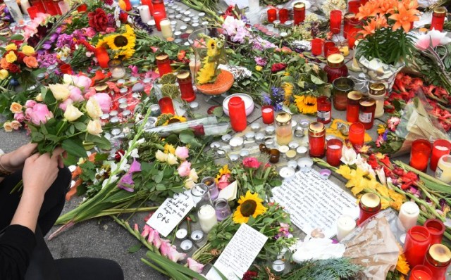 A person mourns in front of candles and flowers on July 25, 2016 near the Olympia shopping mall in Munich, southern Germany, where an 18-year-old German-Iranian student run amok.  Europe reacted in shock to the third attack on the continent in just over a week, after David Ali Sonboly went on a shooting spree at a shopping centre on July 22, 2016 in what appears to have been a premeditated attack, before turning the gun on himself.  / AFP PHOTO / CHRISTOF STACHE