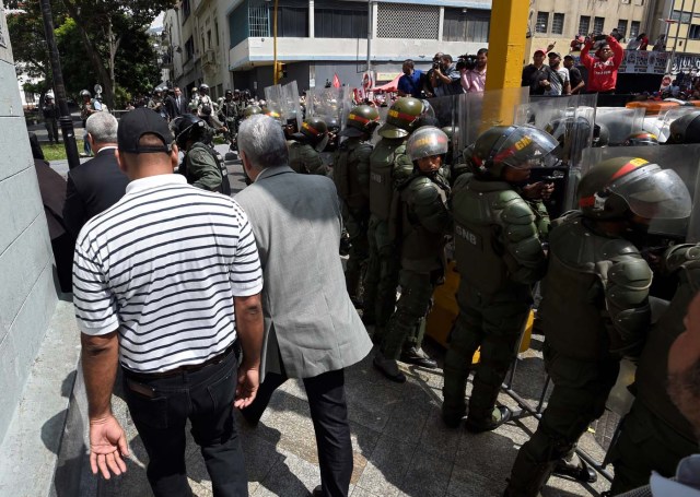 Opposition lawmakers protect themselves while they try to reach the National Assembly in Caracas on October 27, 2016. "We are going to notify Nicolas Maduro that the Venezuelan people declare he has abandoned his post," the speaker of the National Assembly, Henry Ramos Allup, said to cheers from hordes of protesters in Caracas. / AFP PHOTO / JUAN BARRETO