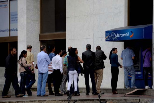 People queue to withdraw money from an automated teller machine (ATM) in Caracas on December 1, 2016. Venezuelan banks guaranteed their continued operation, after rumors about a close in December to adjust to an alleged issuance of bills of higher denomination. At the moment, the note of highest denomination is the one of 100 bolivars, that is just enough to buy a sweet. / AFP PHOTO / Federico PARRA