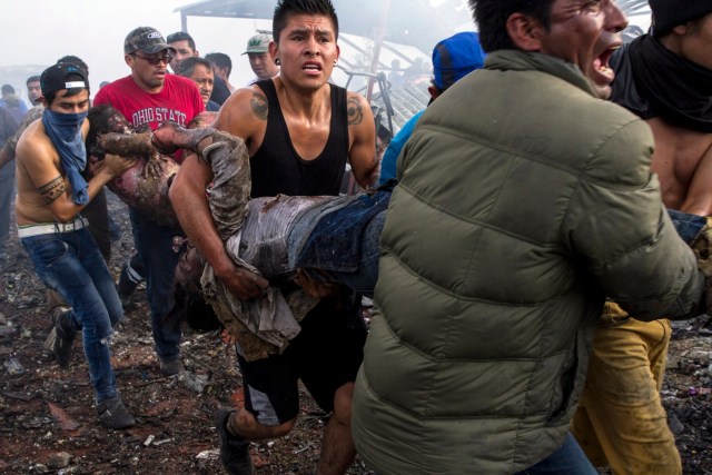 Victims severely burnt are taken away from the smoldering ruins of a fireworks market, flattened by a huge blast that killed at least 31 and injured dozens, in Mexico City, on December 20, 2016. A massive explosion gutted Mexico's biggest fireworks market on Tuesday, killing at least 31 people and injuring 72, the authorities said. The conflagration in the Mexico City suburb of Tultepec set off a quick-fire series of multicolored blasts that sent a vast cloud of smoke billowing over the capital. / AFP PHOTO / ISRAEL GUTIERREZ / GRAPHIC CONTENT