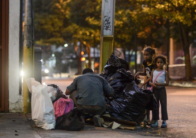 A man scavenges for food next to girls in the streets of Caracas on February 21, 2017. Venezuelan President Nicolas Maduro is resisting opposition efforts to hold a vote on removing him from office. The opposition blames him for an economic crisis that has caused food shortages. / AFP PHOTO / JUAN BARRETO / TO GO WITH AFP STORY BY Alexander Martinez
