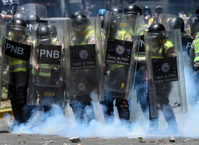 Bolivarian police agents use their shields to protect themselves during clashes with Nicolas Maduro's government opposition activists   in Caracas on April 4, 2017. Protesters clashed with police in Venezuela Tuesday as the opposition mobilized against moves to tighten President Nicolas Maduro's grip on power. Protesters hurled stones at riot police who fired tear gas as they blocked the demonstrators from advancing through central Caracas, where pro-government activists were also planning to march.  / AFP PHOTO / JUAN BARRETO