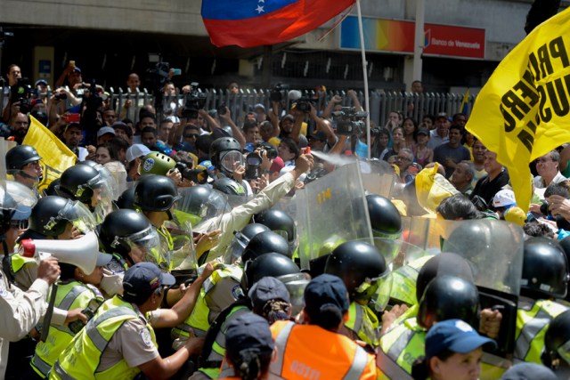 Opposers clash with riot police during a protest against President Nicolas Maduro's government in Caracas on April 4, 2017.  Activists clashed with police in Venezuela Tuesday as the opposition mobilized against moves to tighten President Nicolas Maduro's grip on power. Protesters hurled stones at riot police who fired tear gas as they blocked the demonstrators from advancing through central Caracas, where pro-government activists were also planning to march. / AFP PHOTO / FEDERICO PARRA