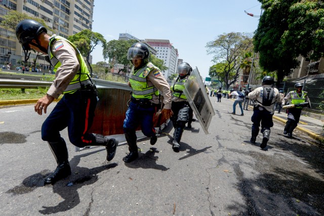 Riot police clear the street of debris during a protest against President Nicolas Maduro's government in Caracas on April 4, 2017.  Activists clashed with police in Venezuela Tuesday as the opposition mobilized against moves to tighten President Nicolas Maduro's grip on power. Protesters hurled stones at riot police who fired tear gas as they blocked the demonstrators from advancing through central Caracas, where pro-government activists were also planning to march. / AFP PHOTO / FEDERICO PARRA