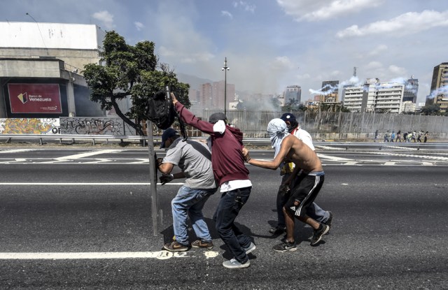 Demonstrators take cover as riot police fire tear gas grenades ad rubber bullets at them during a protest against President Nicolas Maduro's government in Caracas on April 4, 2017.  Activists clashed with police in Venezuela Tuesday as the opposition mobilized against moves to tighten President Nicolas Maduro's grip on power. Protesters hurled stones at riot police who fired tear gas as they blocked the demonstrators from advancing through central Caracas, where pro-government activists were also planning to march. / AFP PHOTO / JUAN BARRETO