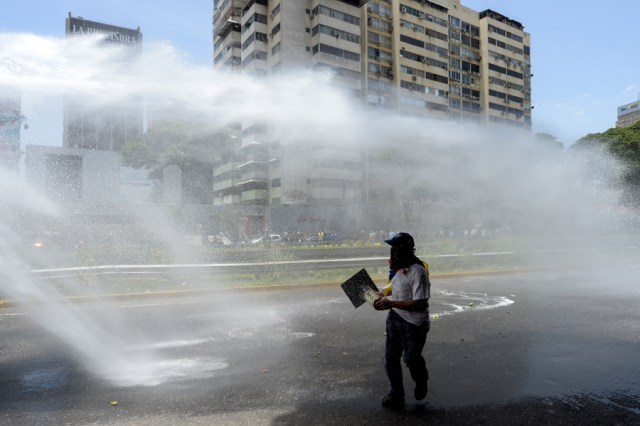 A riot police water cannon sprays opposition activists protesting against President Nicolas Maduro's government in Caracas on April 4, 2017.  Activists clashed with police in Venezuela Tuesday as the opposition mobilized against moves to tighten President Nicolas Maduro's grip on power. Protesters hurled stones at riot police who fired tear gas as they blocked the demonstrators from advancing through central Caracas, where pro-government activists were also planning to march. / AFP PHOTO / FEDERICO PARRA
