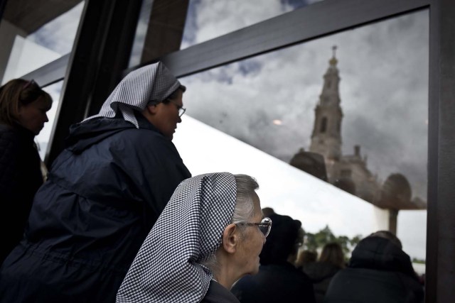 Two nuns outside the chapel "Capelinha das Aparicoes" attend a mass as the "Nossa Senhora do Rosario de Fatima" cathedral's spire is reflected on the window at Fatima, central Portugal, on May 11, 2017. Two of the three child shepherds who reported apparitions of the Virgin Mary in Fatima, Portugal, one century ago, will be declared saints on May 13, 2017 by Pope Francis. The canonisation of Jacinta and Francisco Marto will take place during the Argentinian pontiff's visit to a Catholic shrine visited by millions of pilgrims every year. / AFP PHOTO / PATRICIA DE MELO MOREIRA