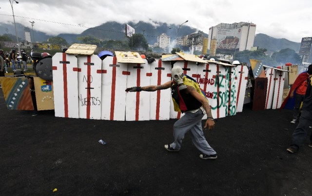 Opposition activists take refuge behind shields in clashes with police during a demonstration against the government of Venezuelan President Nicolas Maduro in front of the Francisco de Miranda air force base in Caracas on June 24, 2017, near the place where a young man was shot dead by police during an anti-government rally two days ago. A political and economic crisis in the oil-producing country has spawned often violent demonstrations by protesters demanding Maduro's resignation and new elections. The unrest has left 75 people dead since April 1. / AFP PHOTO / JUAN BARRETO