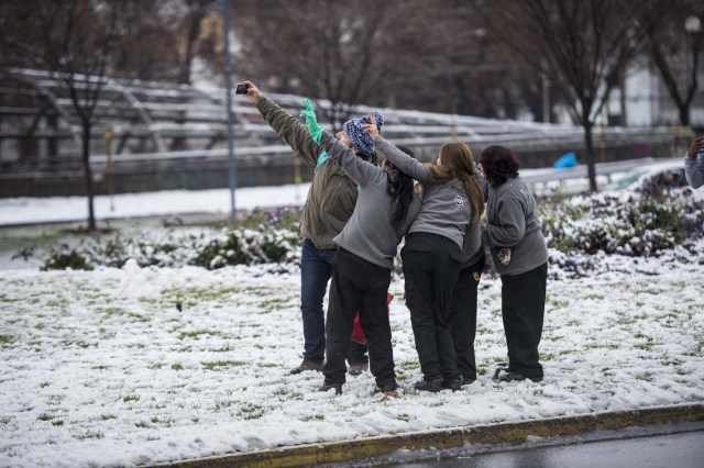 People pose for a selfie during a snowfall in Santiago on July 15, 2017.  An unusual snowfall --the first of such intensity since 2007-- surprised the inhabitants of the Chilean capital, causing a few power cuts and minor traffic jams, in particular in the eastern areas of the capital, the closest to the Andes mountain range. / AFP PHOTO / Martin BERNETTI