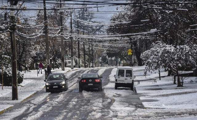 Cars drive along a street covered with snow in Santiago on July 15, 2017.  An unusual snowfall --the first of such intensity since 2007-- surprised the inhabitants of the Chilean capital, causing a few power cuts and minor traffic jams, in particular in the eastern areas of the capital, the closest to the Andes mountain range. / AFP PHOTO / Martin BERNETTI