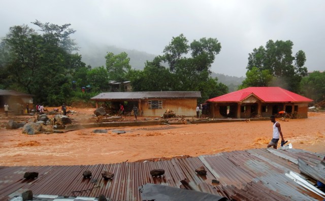 A resident walks through floodwaters past a damaged building in an area of Freetown on August 14, 2017, after landslides struck the capital of the west African state of Sierra Leone. At least 312 people were killed and more than 2,000 left homeless when heavy flooding hit Sierra Leone's capital of Freetown, leaving morgues overflowing and residents desperately searching for loved ones. An AFP journalist at the scene saw bodies being carried away and houses submerged in two areas of the city, where roads turned into churning rivers of mud and corpses were washed up on the streets. / AFP PHOTO / SAIDU BAH