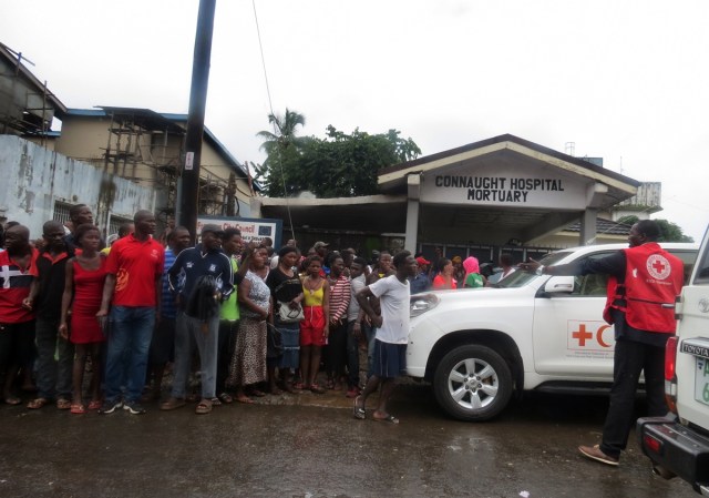 Bystanders look on as emergency personnel gather at the entrance to the mortuary of Connaught Hospital in Freetown on August 14, 2017, after landslides struck the capital of the west African state of Sierra Leone. At least 312 people were killed and more than 2,000 left homeless when heavy flooding hit Sierra Leone's capital of Freetown, leaving morgues overflowing and residents desperately searching for loved ones. An AFP journalist at the scene saw bodies being carried away and houses submerged in two areas of the city, where roads turned into churning rivers of mud and corpses were washed up on the streets. / AFP PHOTO / SAIDU BAH