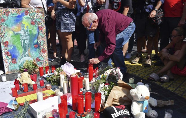 A man holds a candle next to other items set up on the Las Ramblas boulevard in Barcelona as they pay tribute to the victims of the Barcelona attack, a day after a van ploughed into the crowd, killing 13 persons and injuring over 100 on August 18, 2017. Police hunted for the driver who rammed a van into pedestrians on an avenue crowded with tourists in Barcelona, leaving 13 people dead and  more than 100 injured, just hours before a second assault in a resort along the coast. / AFP PHOTO / Pascal GUYOT
