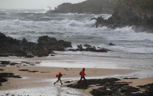 People walk across a beach as storm Ophelia approaches near Trearddur Bay in Anglesey, Wales, Britain, October 16, 2017. REUTERS/Phil Noble