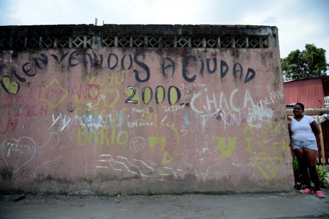 Una mujer se encuentra junto a un muro que dice "Bienvenido a Ciudad 2000" en City 2000, un barrio marginal que alberga a personas desplazadas por guerras territoriales entre bandas criminales en el municipio de Tumaco, departamento de Nariño, Colombia, el 2 de noviembre de 2017. En el remoto municipio de Tumaco, en la región costera del Pacífico colombiano, las pocas familias que no han huido viven con un temor constante a la violencia, a pesar del acuerdo de paz firmado en noviembre de 2016 entre el gobierno y los rebeldes de las FARC, debido a grupos armados que disputan la droga los corredores de tráfico a los Estados Unidos. / AFP PHOTO / Raul Arboleda