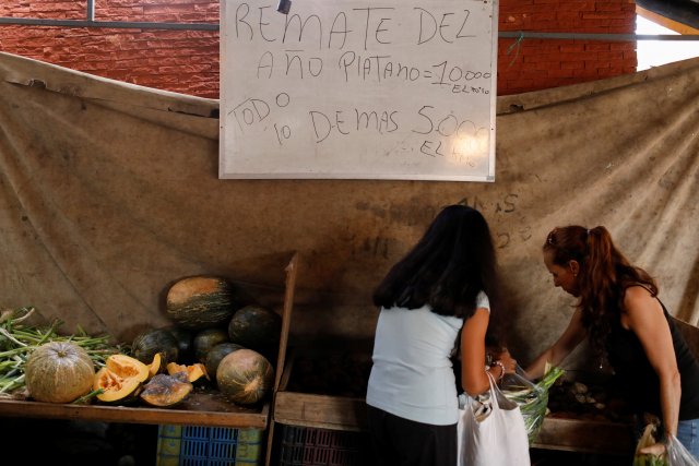 La gente compra en un mercado callejero vegetal frente a una pizarra que dice "Subasta del año. Plátano 10.000 Bolívares por Kg. Todo lo demás 5.000 Bolívares por Kg", en Caracas, Venezuela, 19 de diciembre de 2017. Fotografía tomada el 19 de diciembre de 2017. REUTERS / Marco Bello