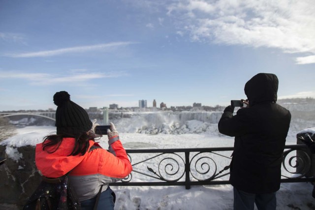 Tourists take photos of the nearly frozen American side of Niagara Falls from Niagara Falls, Ontario on January 3, 2018. The cold snap which has gripped much of Canada and the United States has nearly frozen over the American side of the falls. / AFP PHOTO / Geoff Robins