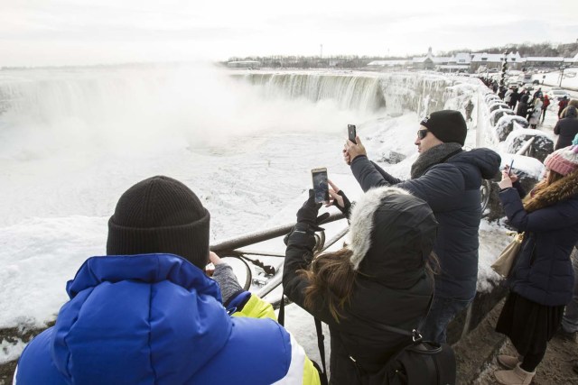 Tourists take photos of the Horseshoe Falls in Niagara Falls, Ontario on January 3, 2018. The cold snap which has gripped much of Canada and the United States has nearly frozen over the American side of the falls. / AFP PHOTO / Geoff Robins