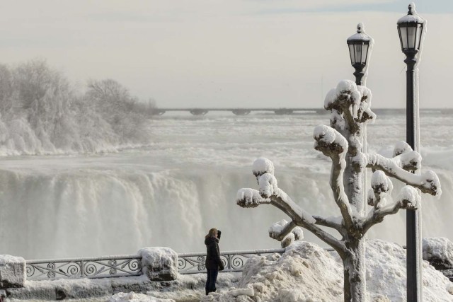 Tourists look out past the frozen railings at the Horseshoe Falls in Niagara Falls, Ontario on January 3, 2018. The cold snap which has gripped much of Canada and the United States has nearly frozen over the American side of the falls. / AFP PHOTO / Geoff Robins