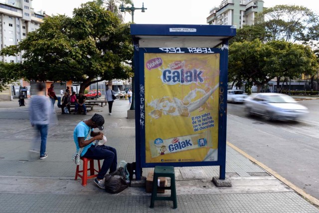 Wilmer Rojas, 25, sists at a bus stop in Caracas as he sews Bolivar bills, to make crafts on January 30, 2018. A young Venezuelan tries to make a living out of devalued Bolivar banknotes by making crafts with them. / AFP PHOTO / FEDERICO PARRA