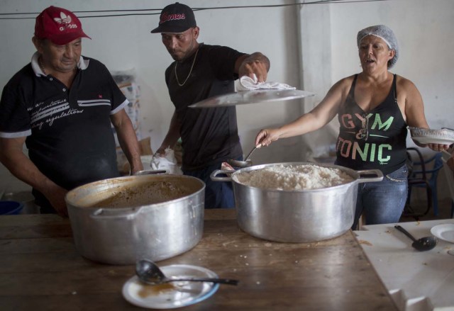 A Venezuelan immigrant (C) helps Brazilian neighborhoods to prepare meals for the Venezuelan refugees living at Simon Bolivar Square, in Boa Vista, Roraima, Brazil, on February 25, 2018. When the Venezuelan migratory flow exploded in 2017 the city of Boa Vista, the capital of the state of Roraima, 200 kilometers from the Venezuelan border, began to set up shelters as people started to settle in squares, parks and corners of this city of 330,000 inhabitants of which 10 percent is now Venezuelan. According to local authorities around one thousand refugees are crossing each day the Brazilian border from Venezuela. / AFP PHOTO / MAURO PIMENTEL