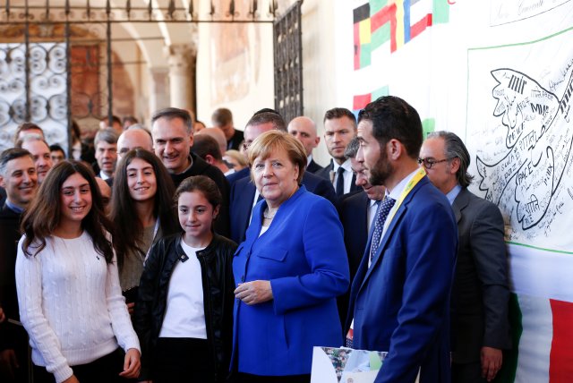 La canciller alemana Angela Merkel posa con los jóvenes después de firmar una bandera de la paz durante su visita a Asís, Italia, el 12 de mayo de 2018. REUTERS / Yara Nardi 