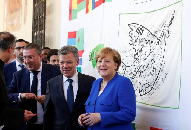 La canciller alemana Angela Merkel y el presidente colombiano Juan Manuel Santos (C) posan junto a una bandera de la Paz durante su visita a Asís, Italia, el 12 de mayo de 2018. REUTERS / Yara Nardi 